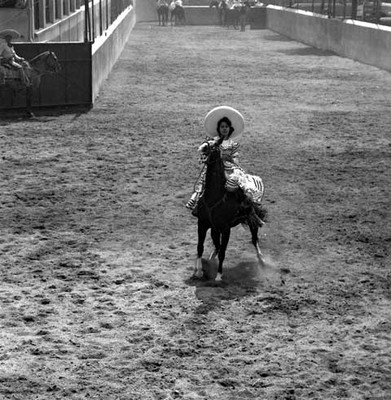 Mujer charra realizando la suerte del rayado a caballo durante una charreada