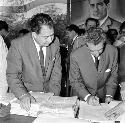 Adolfo López Mateos firmando título agrario acompañado de Carlos A. Madrazo Becerra, durante una ceremonia al aire libre en Cárdenas