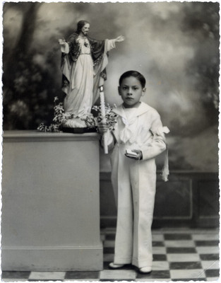 Niño junto a una imagen religiosa, viste traje de primera comunión, retrato
