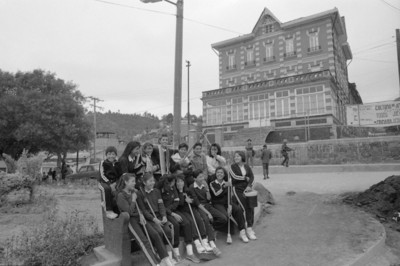 Estudiantes sentados en una banca de jardín, al fondo el antiguo Casino-Hotel de la fábrica San Rafael