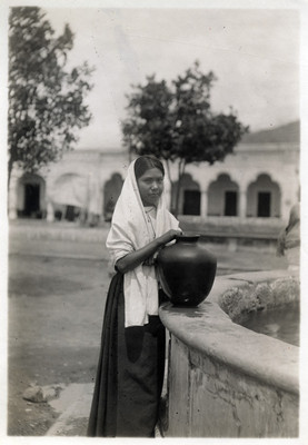 Adolescente indígena junto a una fuente con una olla