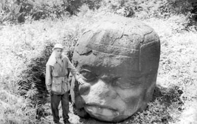 Hombre toca con la amno una cabeza colosal Olmeca