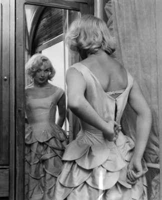 Transexual sube el cierre de la espalda de su vestido frente a un espejo