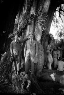 Rafael Quevedo acompañado por un hombre junto al tronco de un árbol, retrato
