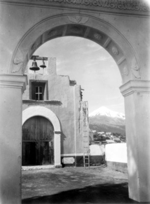 Portón y campanario de una iglesia, al fondo un volcán