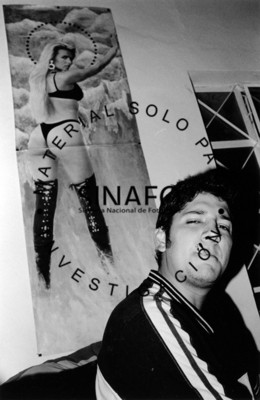 Hombre fuma frente a poster de mujer con traje de baño y botas, retrato