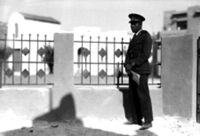 Policía con un documento en la mano, frente a la cerca de una casa habitación