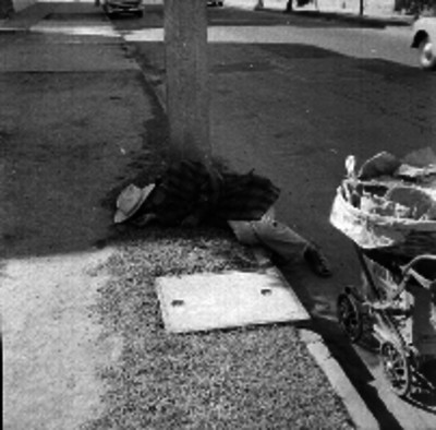Indigente durmiendo en la banqueta de una calle junto a un carrito con desperdicios