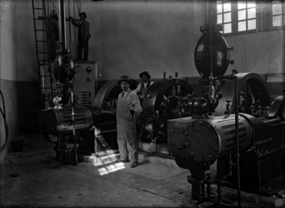 Obreros posan junto a maquinaria, interior de fábrica
