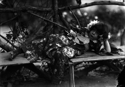 Niña vestida de oriental, tendida sobre la banca de un jardín, en un festival escolar