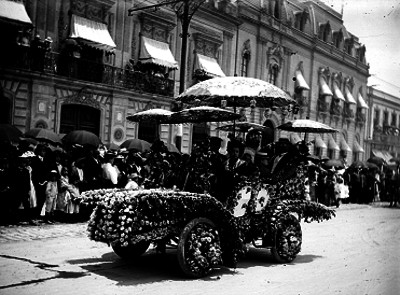 Familia de clase alta en un automóvil adornado con flores y sombrillas estilo Japonés desfilando en una calle