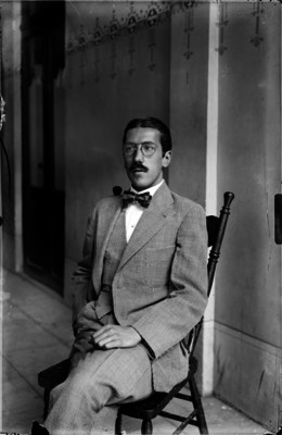 Luis G. Corona, licenciado, sentado en una silla en el corredor de un edificio, retrato