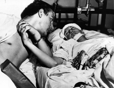 Enferma en cama sujeta de la mano a hombre