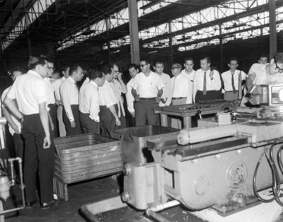 Hombres comentan frente a maquinaria durante visita a planta automotríz