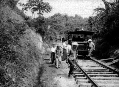 Ferrocarrileros reparan vías férreas, mientras dos mujeres descansan en un armón