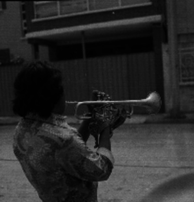 Hombre tocando la trompeta enfrente de una casa en la calle