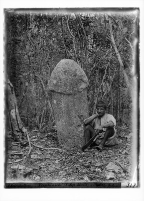 Hombre sentado junto a escultura de piedra de forma fálica
