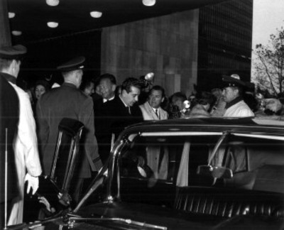 Adolfo López Mateos rodeado por reporteros y otras personas, al salir de un edificio