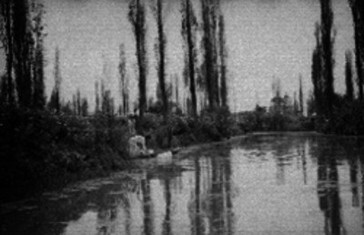 Mujer de condición humilde sobre una trajinera a la orilla de un canal