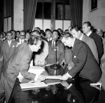 Adolfo López Mateos entregando documentos a un hombre en una ceremonia en un salón, durante su gira de trabajo por Veracruz