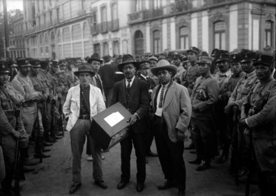 Hombres transportando una urna elctoral escoltados por militares