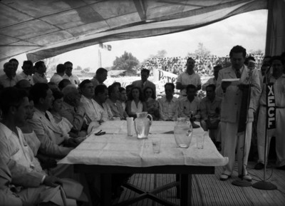 Miguel Alemán Valdés escuchando a un hombre dar lectura de un documento durante una ceremonia