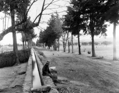 Hombre sentado a la orilla de un canal de riego