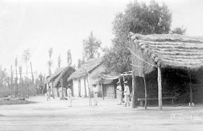 Hombres junto a casas rusticas en el "pueblo de Santa Anita"