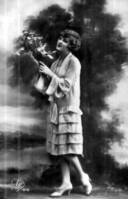 Mujer posa de pie con vestido y sostiene ramo de flores