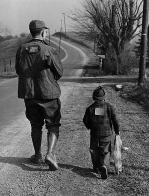Hombre y niño cazadores caminan junto a una carretera